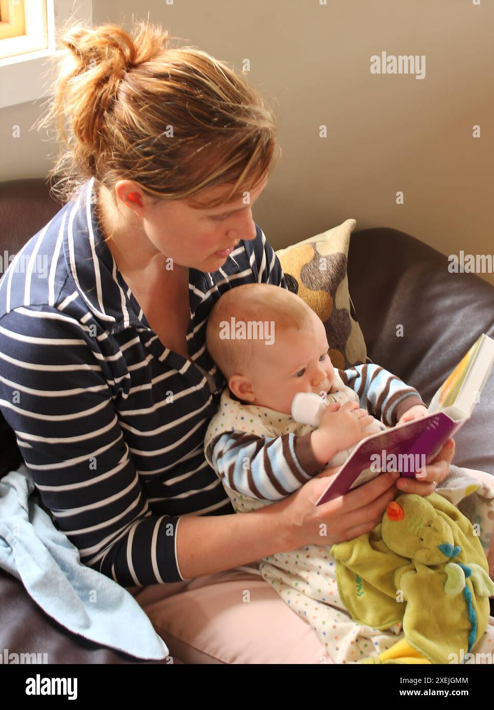 Mère et bébé lisant un livre ensemble sur un canapé Banque D'Images