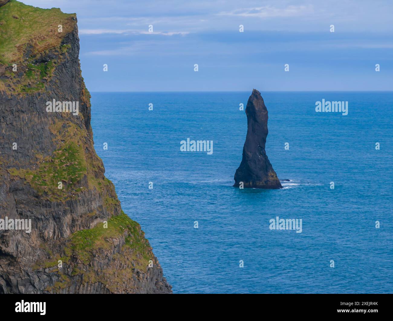 Majestueux Sea Stack s'élevant des eaux de l'océan bleu au large de la côte islandaise Banque D'Images