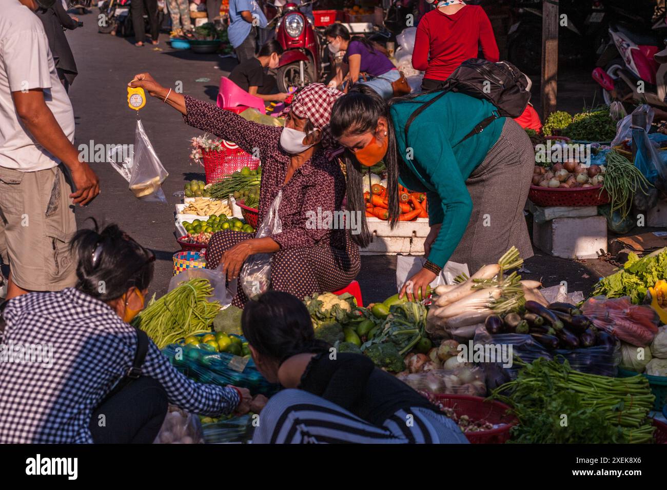 Vendeur de légumes cambodgien portant un masque et utilisant une balance à main pendant la pandémie COVID-19. Le marché russe, Phnom Penh, Cambodge. © Kraig Lieb Banque D'Images