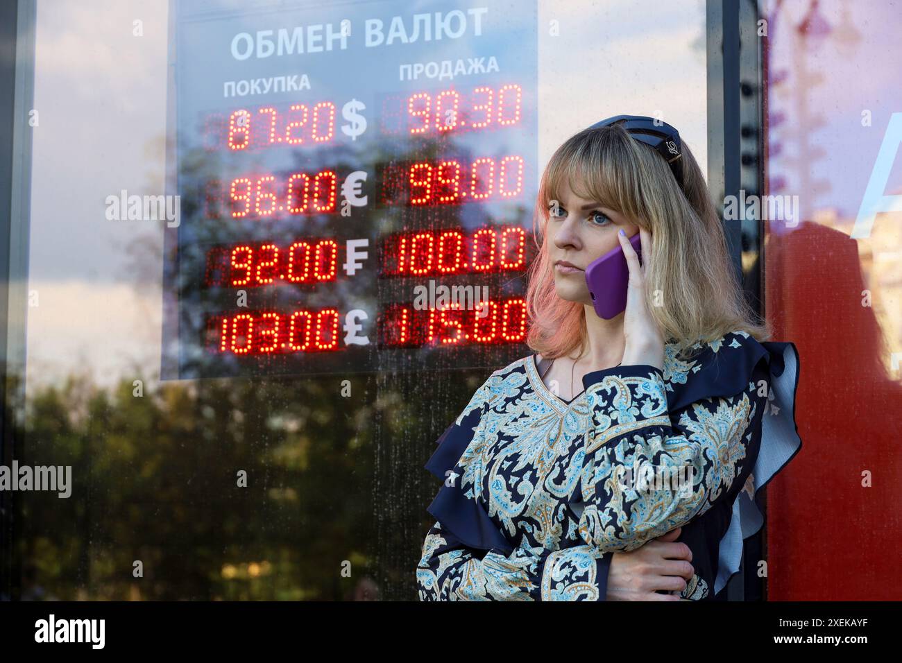 Fille parlant sur le téléphone portable debout près du bureau de change dans la rue de la ville, les taux du rouble russe, dollar américain, euro Banque D'Images