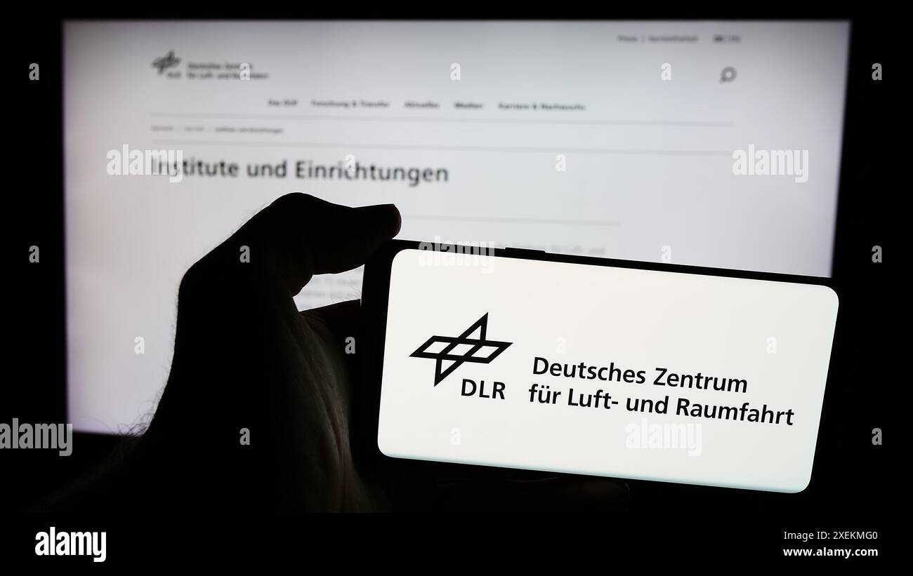 Personne tenant un téléphone portable avec le logo de Deutsches Zentrum für Luft- und Raumfahrt e.V. (DLR) devant la page web. Concentrez-vous sur l'affichage du téléphone. Banque D'Images