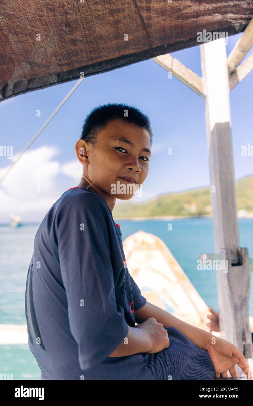 Gros plan portrait informel d'un garçon sur un bateau dans la mer des Moluques au large de la plage de Patokan (Jiko) dans le nord de Sulawesi, Indonésie Banque D'Images