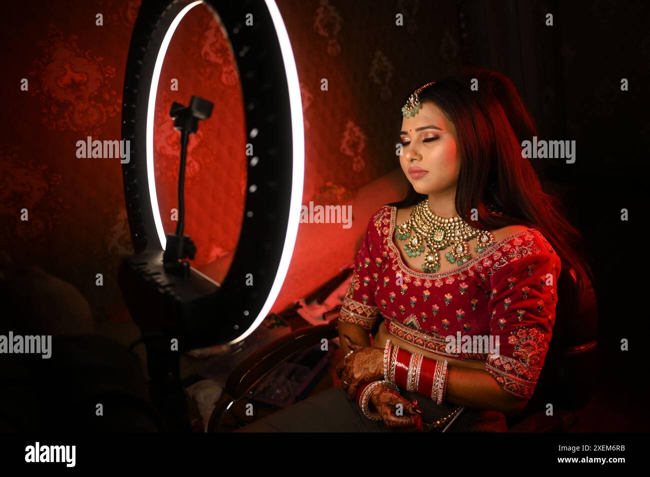 Une mariée indienne en tenue traditionnelle, ornée de bijoux complexes assis les yeux fermés devant un anneau lumineux lumineux Banque D'Images