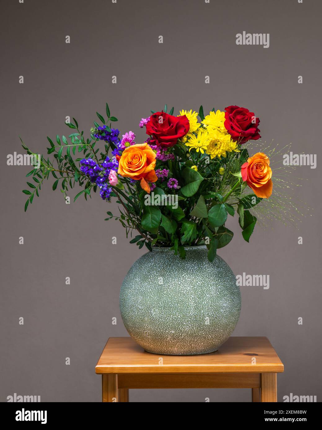 Un bouquet lumineux et coloré de fleurs dans un vase gris sur une table en bois sur un fond gris clair Banque D'Images