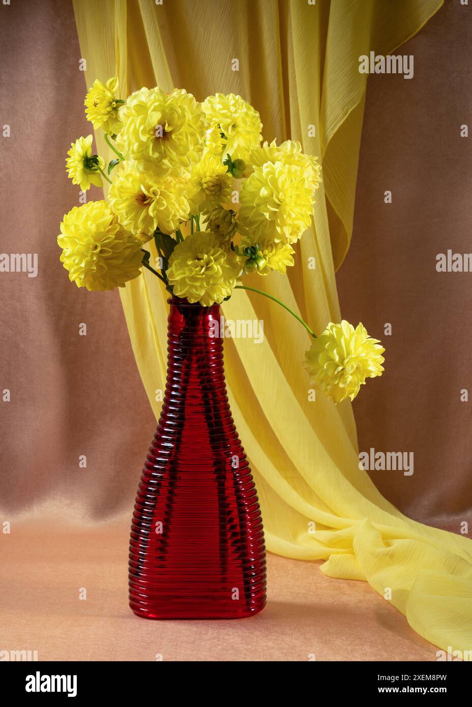 Bouquet de dahlias jaunes dans un vase en verre rouge sur la table. Calme Banque D'Images