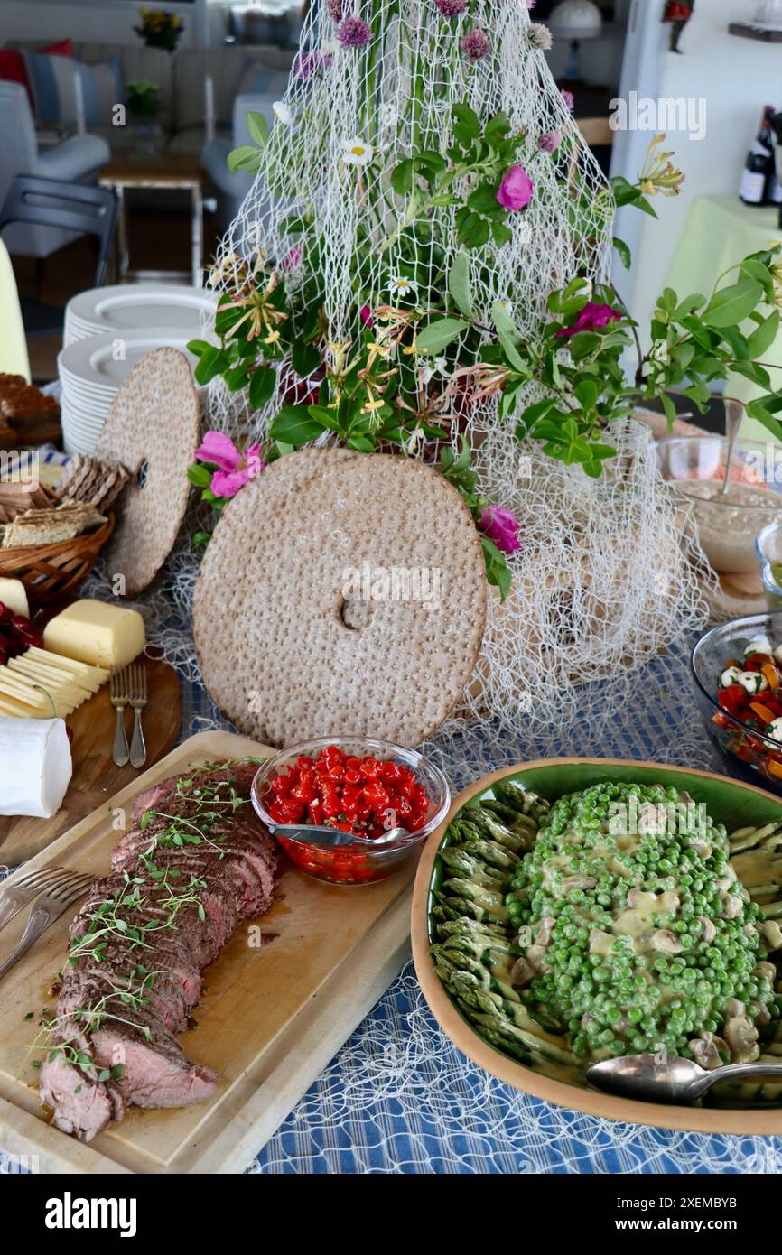 Dîner buffet décoré d'un vieux filet de pêche, de roses sauvages et de fleurs d'oignons sauvages. Mi-été en Suède, juin 2024 Banque D'Images