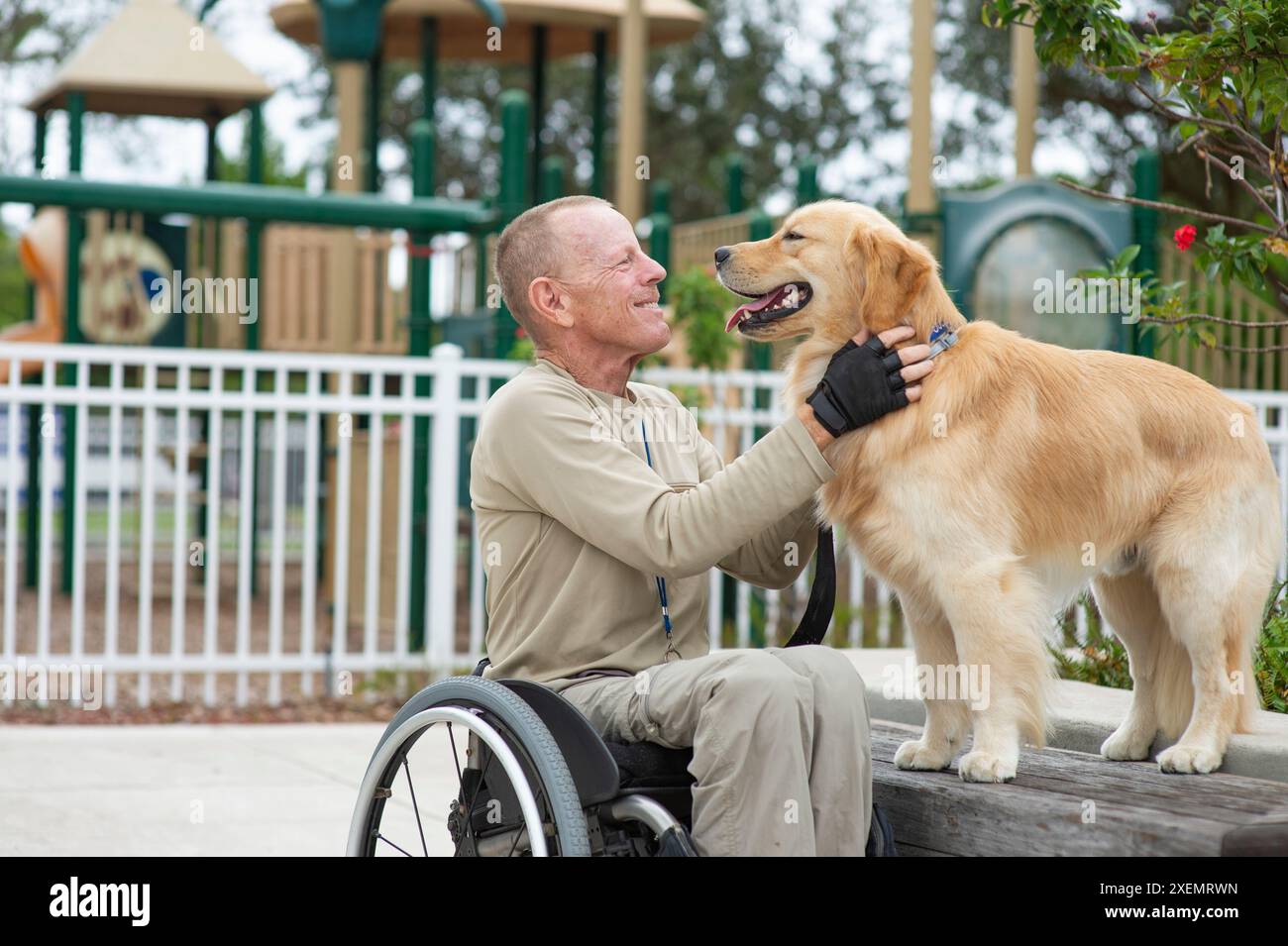 Homme en fauteuil roulant appréciant le temps avec son chien d'assistance dans un parc ; Boynton Beach, Floride, États-Unis d'Amérique Banque D'Images