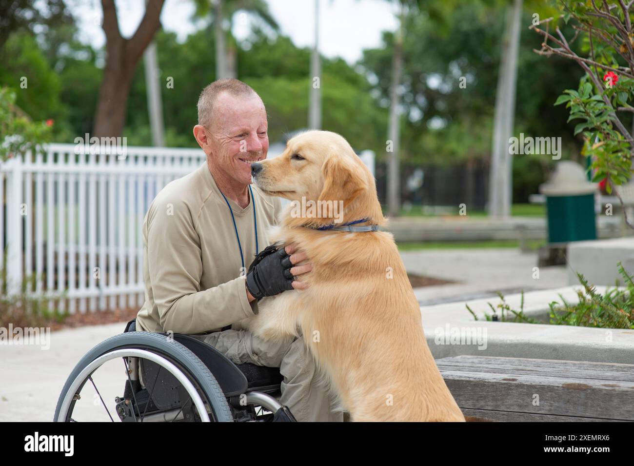 Homme en fauteuil roulant passant du temps avec son chien d'assistance dans un parc de la ville ; Boynton Beach, Floride, États-Unis d'Amérique Banque D'Images