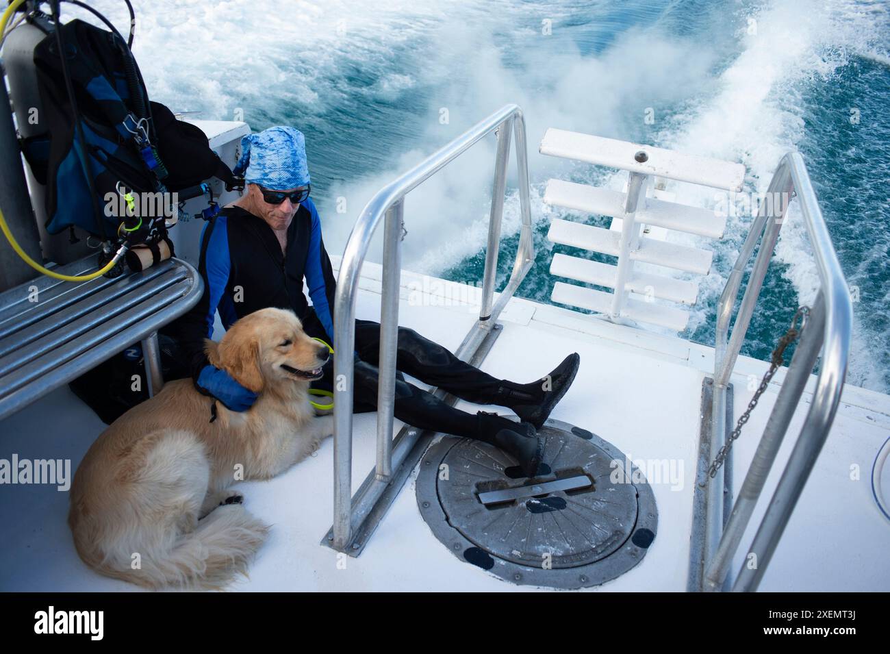 Homme paraplégique et son chien d'assistance chevauchant ensemble à l'arrière d'un bateau de plongée avec le réveil du bateau visible derrière eux Banque D'Images