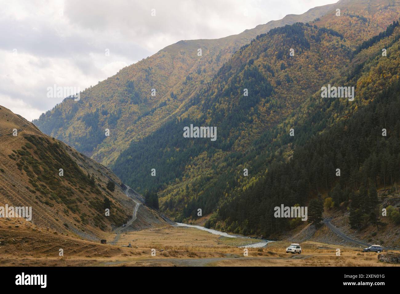 Véhicules sur un col de montagne près du village de Dartlo dans le parc national de Tusheti, avec des arbres aux couleurs d'automne sur le flanc de la montagne Banque D'Images