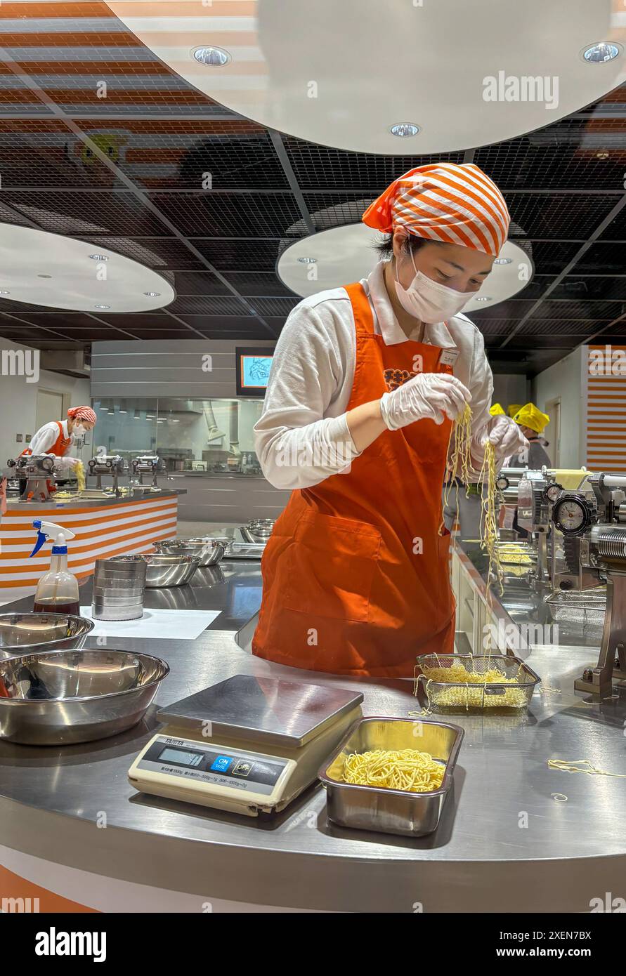 Un membre du personnel du musée CupNoodles vérifie les nouilles pendant le processus de production des nouilles instantanées et essaie de faire leurs propres nouilles instantanées personnalisées. Le musée est dédié à l'histoire des nouilles instantanées et à l'histoire de Nissin Foods, fondée par Momofuku Ando, l'inventeur des nouilles instantanées et des CupNoodles. Le musée a deux emplacements, l'un à Osaka et l'autre à Yokohama, au Japon. Banque D'Images