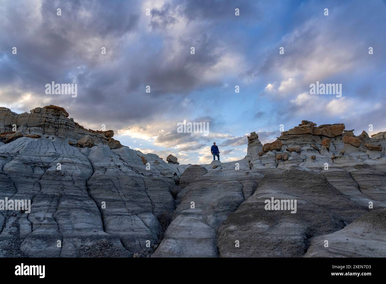 Vue en angle bas d'un homme debout au sommet de formations rocheuses accidentées sous un grand ciel nuageux dans Valley of Dreams, Nouveau-Mexique, États-Unis Banque D'Images