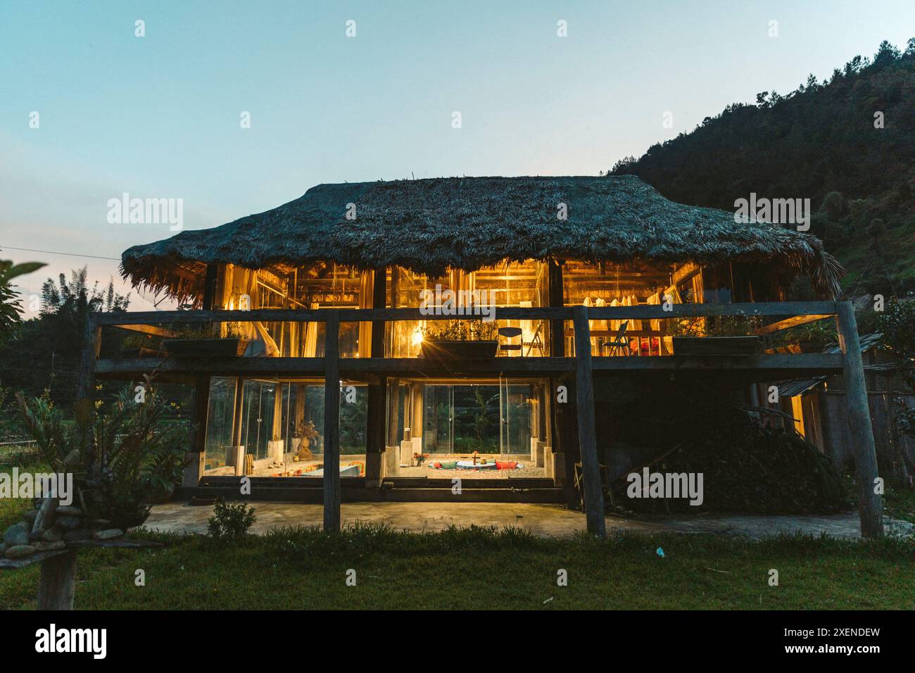Maison de deux étages avec toit de chaume dans la campagne du Vietnam, avec des lumières allumées pour éclairer les chambres au crépuscule Banque D'Images