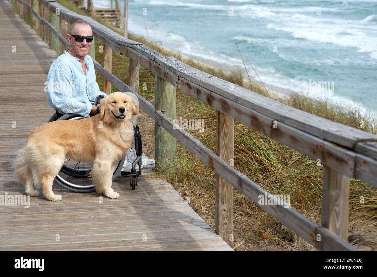 Homme paraplégique en fauteuil roulant avec chien d'assistance profite de la vue sur l'océan depuis une promenade ; Boynton Beach, Floride, États-Unis d'Amérique Banque D'Images