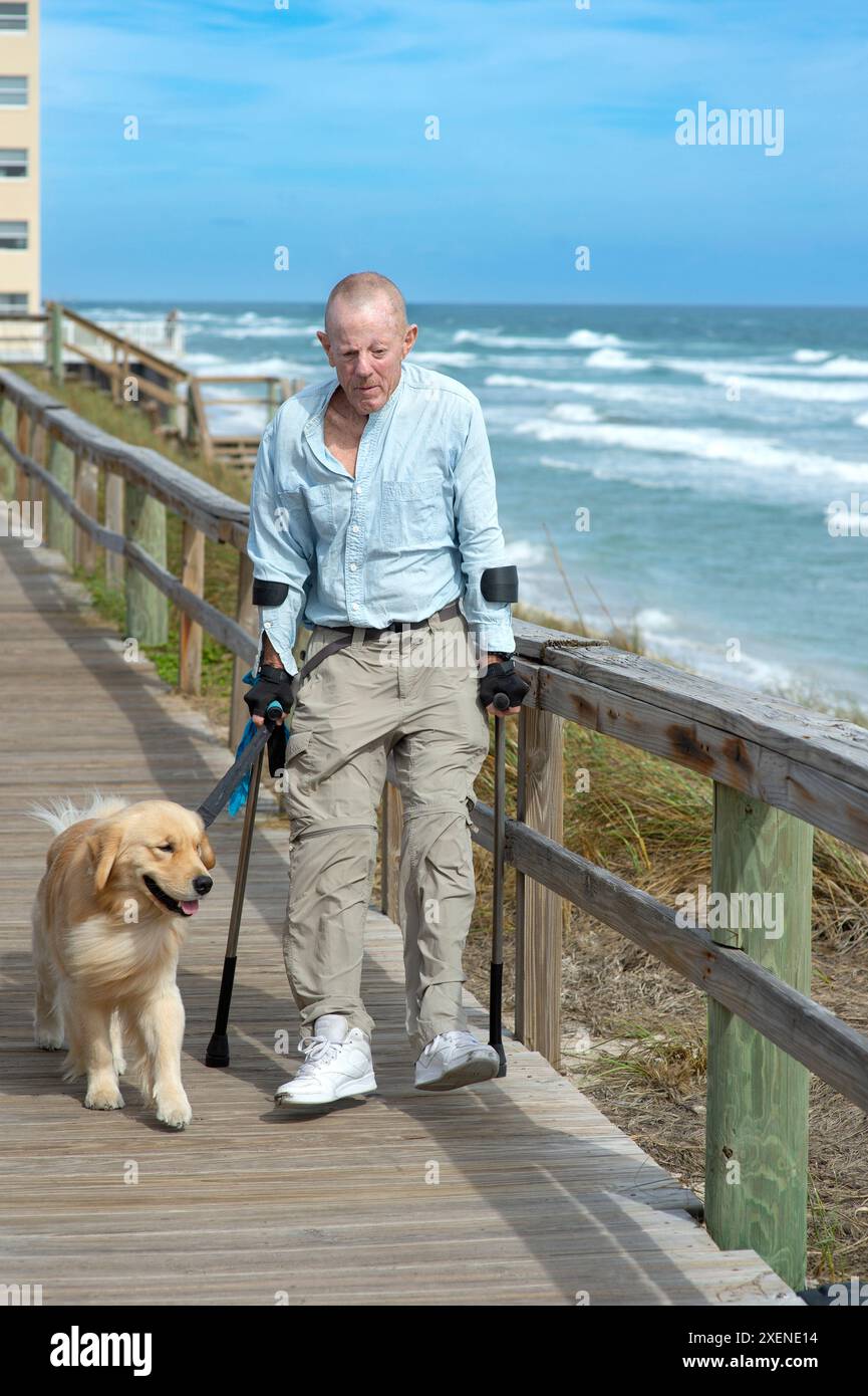 Homme paraplégique avec des béquilles d'avant-bras et chien d'assistance aime marcher le long de la promenade de l'océan ; Boynton Beach, Floride, États-Unis d'Amérique Banque D'Images