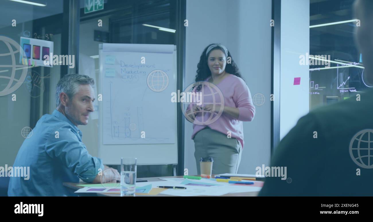Image d'icônes de globe Web flottant contre la femme biraciale donnant une présentation au bureau Banque D'Images