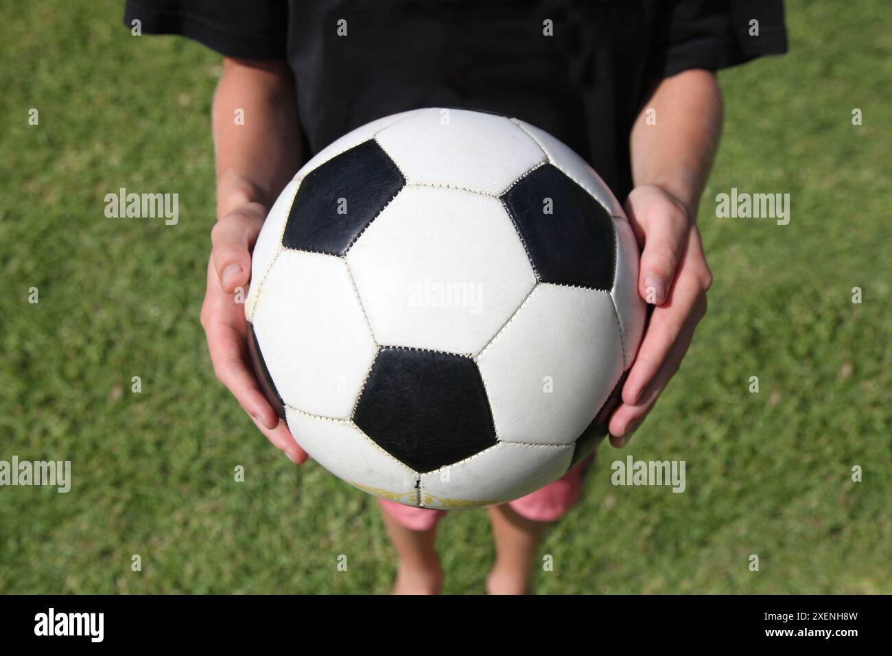 Un garçon tient un ballon de football au-dessus de l'herbe verte Banque D'Images