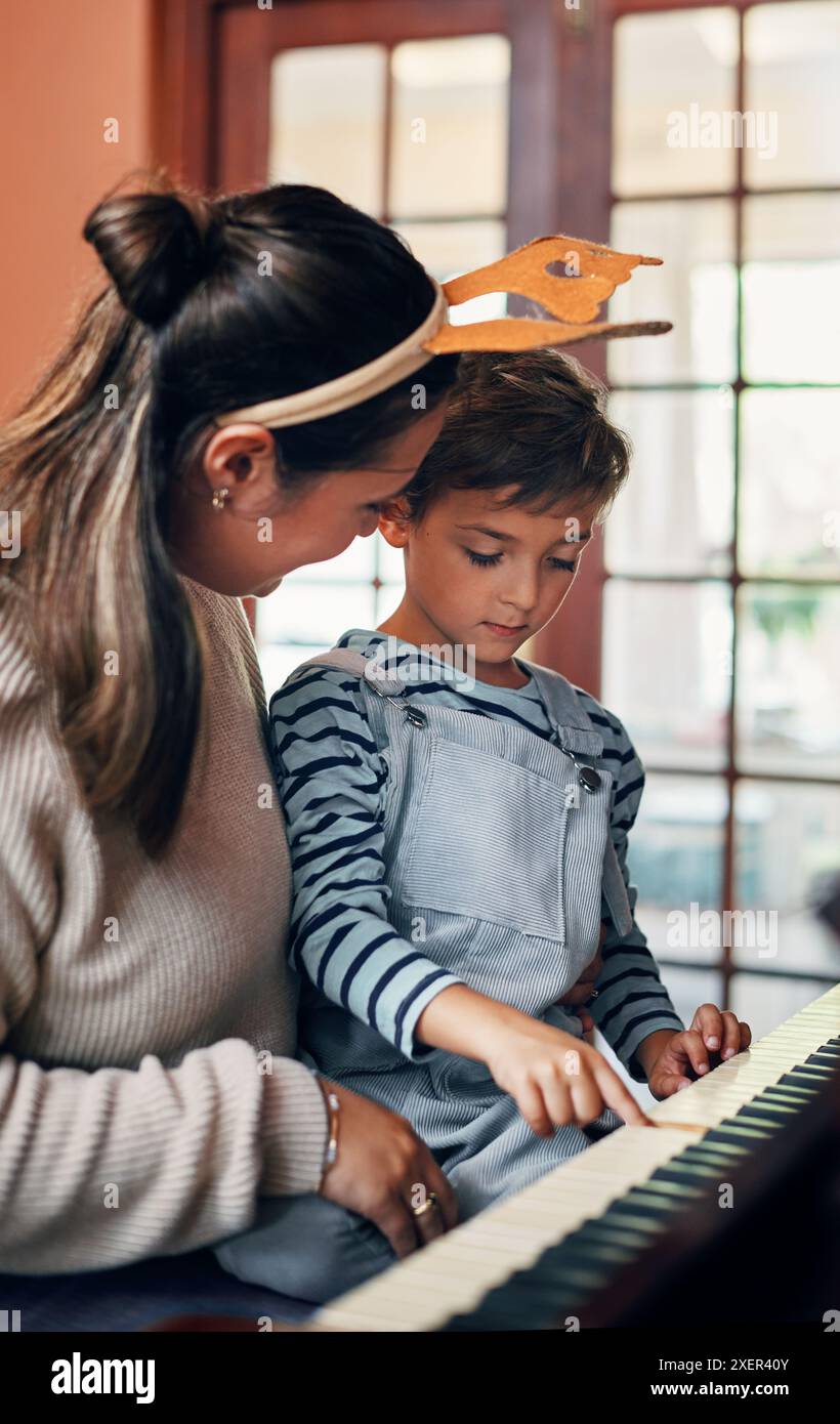 Maman, garçon et piano à Noël à la maison pour carol, chanson ou apprentissage pour la musique, performance ou notes. Mère, enfant ou fils par clavier pour l'enseignement Banque D'Images