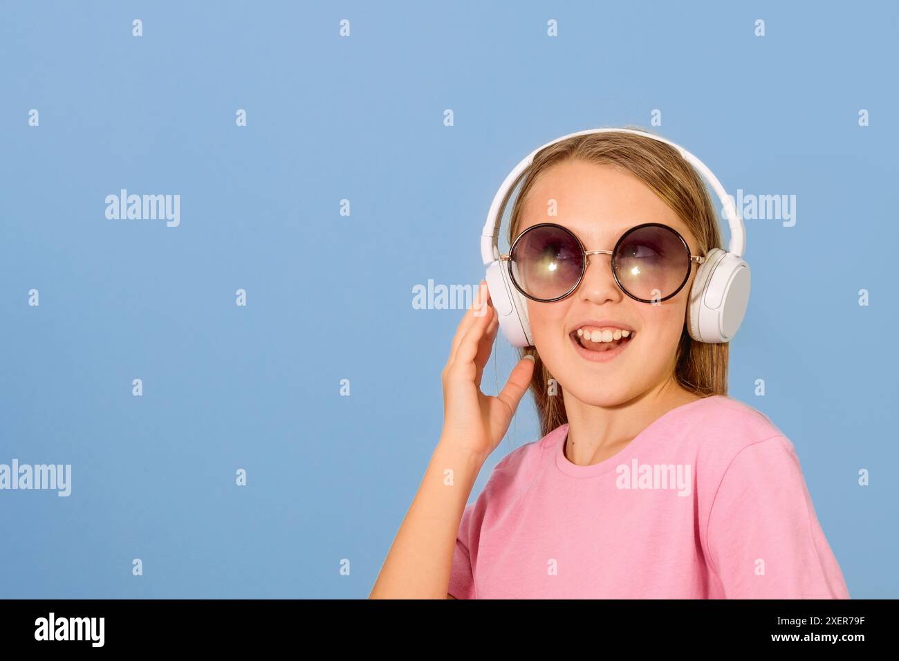 Сheerful fille de 10-12 ans portant des écouteurs. Indique un espace pour le texte. Fond bleu. Copier l'espace Banque D'Images