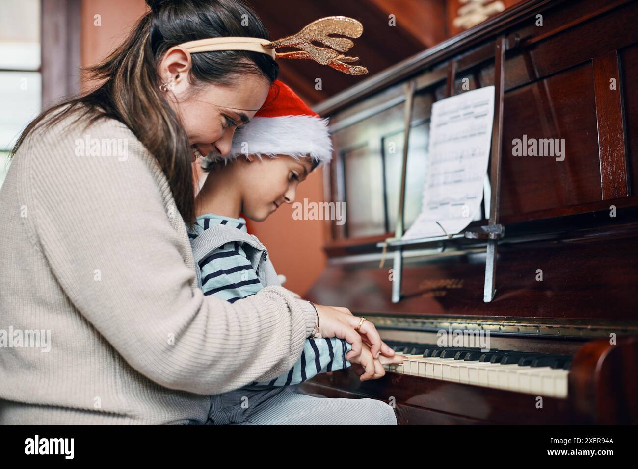 Mère, garçon et piano à Noël à la maison avec le sourire, l'amour ou l'apprentissage pour la musique, la performance ou les notes. Maman, enfant ou fils par clavier pour l'enseignement Banque D'Images