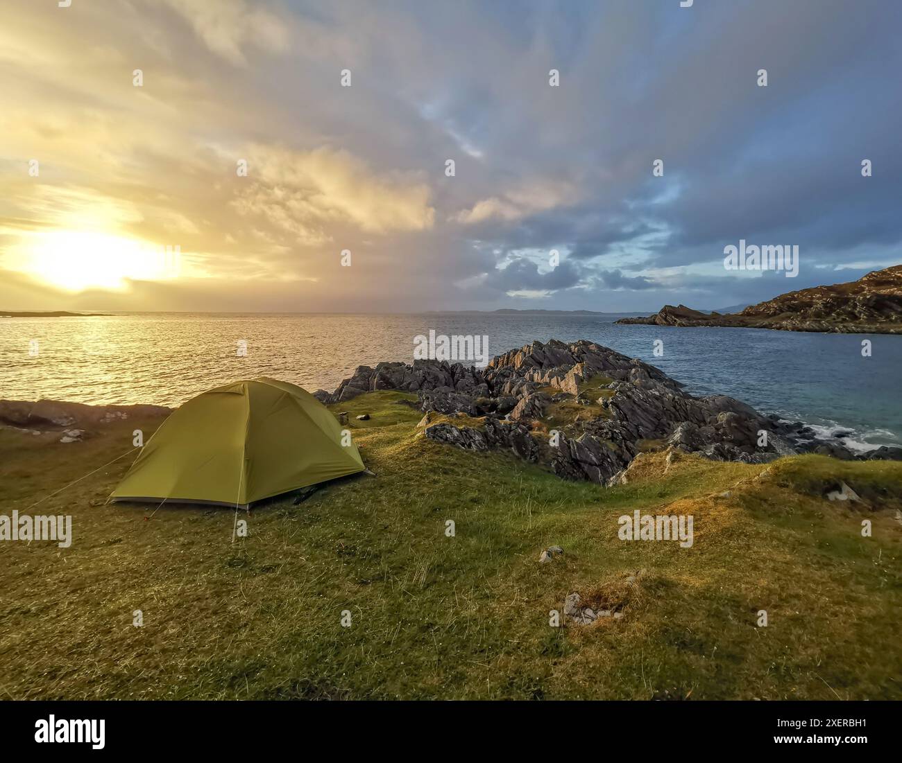 Tente verte camping sauvage sur une rive herbeuse et rocheuse au coucher du soleil à Smirisary, près de Glenuig, côte ouest de l'Écosse Banque D'Images