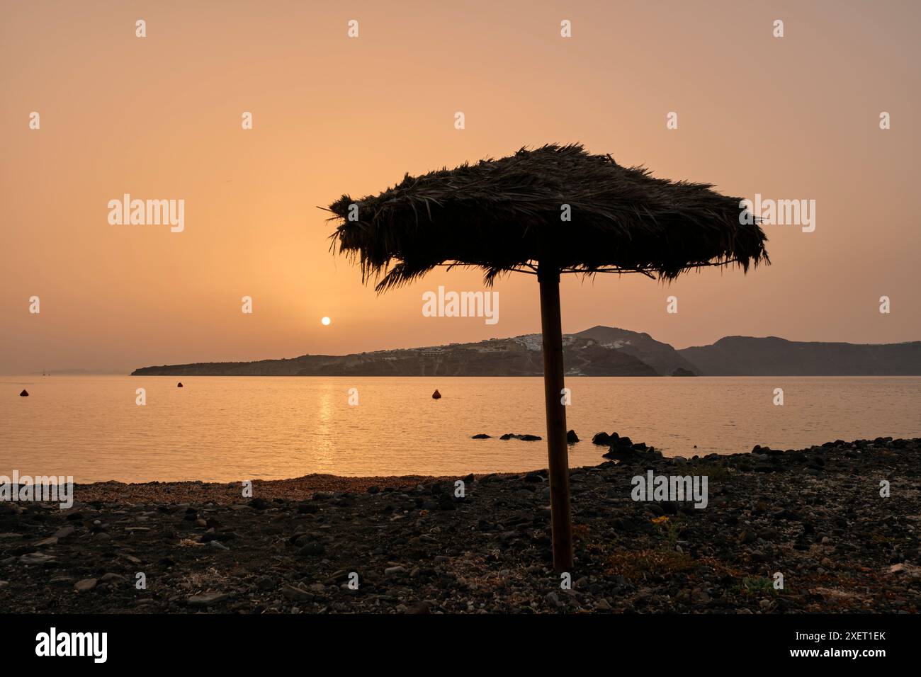Parasol sur la plage de Riva au lever du soleil, avec Santorin en distance. Thirasia, Îles Cyclades, Grèce. Banque D'Images