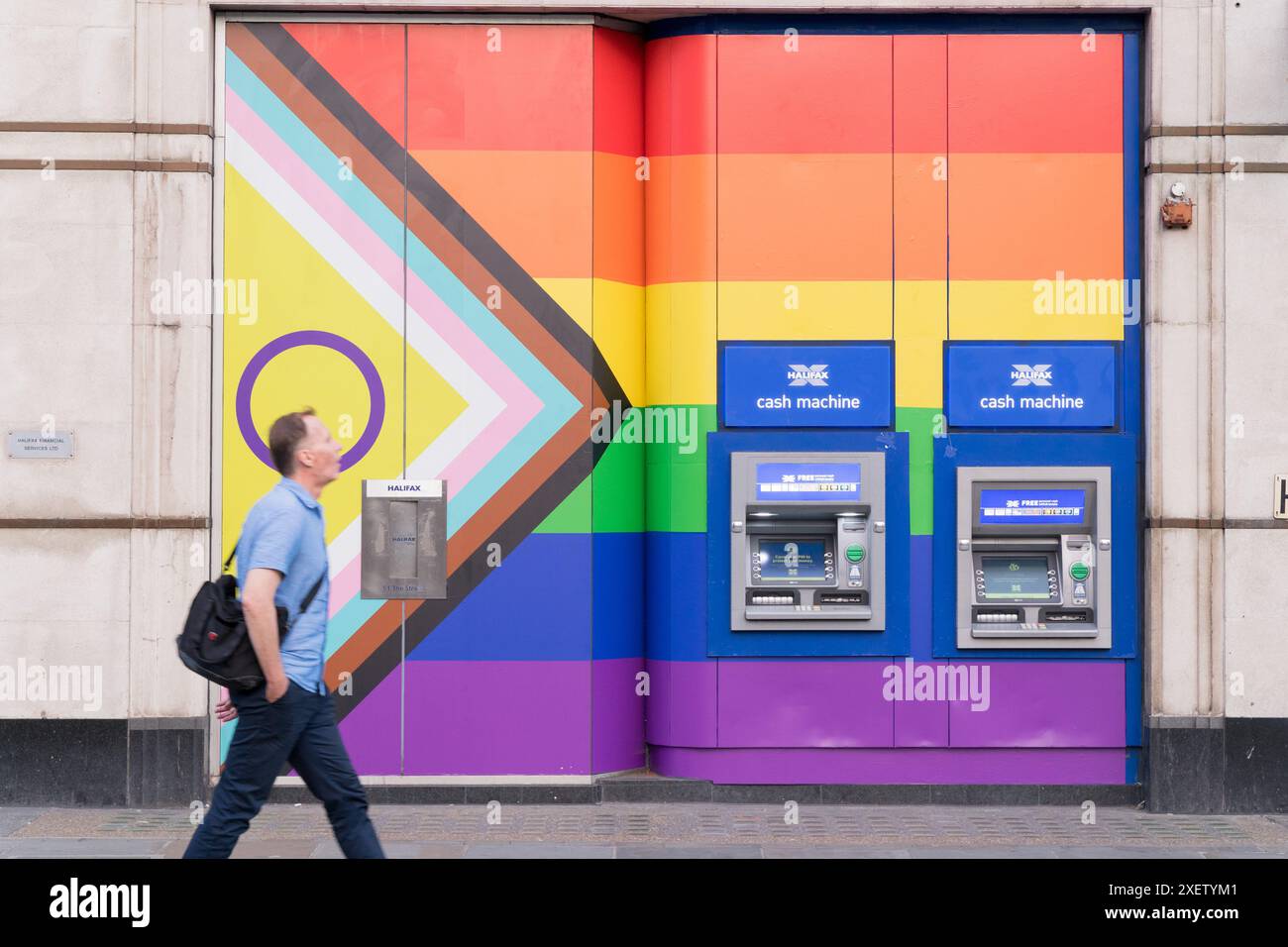 Un homme passe devant deux distributeurs automatiques de billets sur le mur peint avec des couleurs arc-en-ciel pendant la célébration du mois de la fierté en Angleterre Banque D'Images