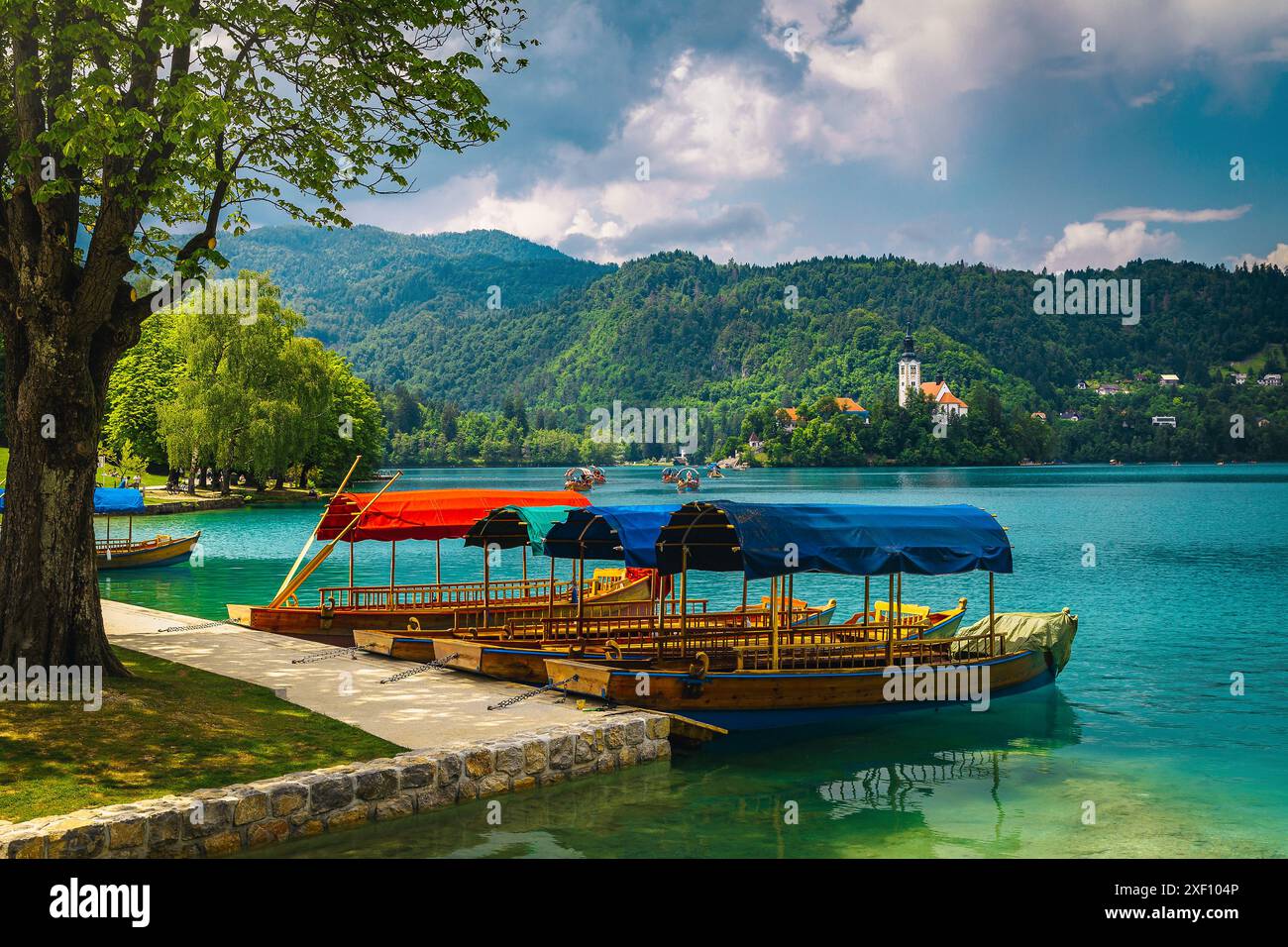 Bateaux Pletna ancrés sur le lac. Bateaux à rames Pletna en bois et église traditionnelle en arrière-plan sur la petite île, Bled, Slovénie, Europe Banque D'Images