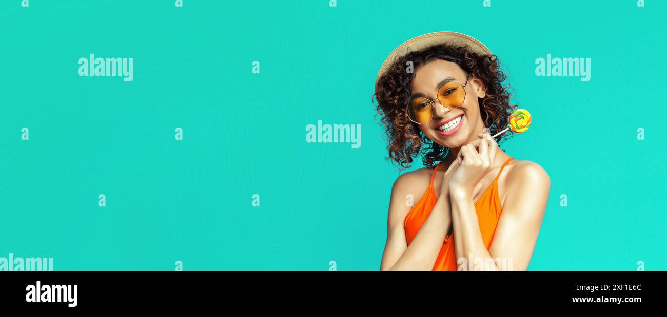 Femme souriante avec cheveux bouclés tenant Lollipop sur fond bleu Banque D'Images