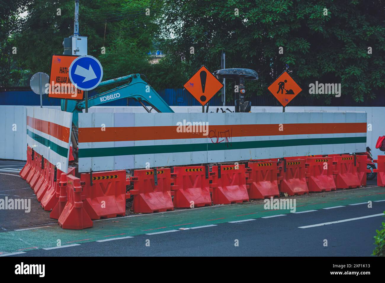 Jakarta, Indonésie - 11 mai 2024. un chantier de réparation de route avec une pelle verte en arrière-plan. Une clôture de sécurité orange entoure la perche Banque D'Images