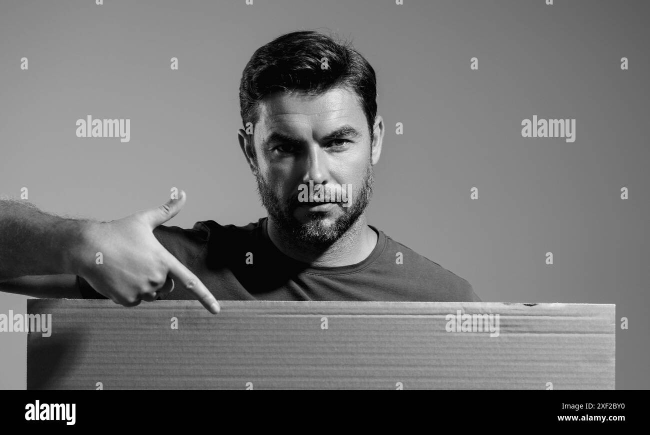 Homme avec une bannière vierge isolée sur l'arrière-plan du studio. Portrait d'un homme attrayant avec une affiche vierge vide. Homme montrant l'affiche, pointant le doigt dessus Banque D'Images