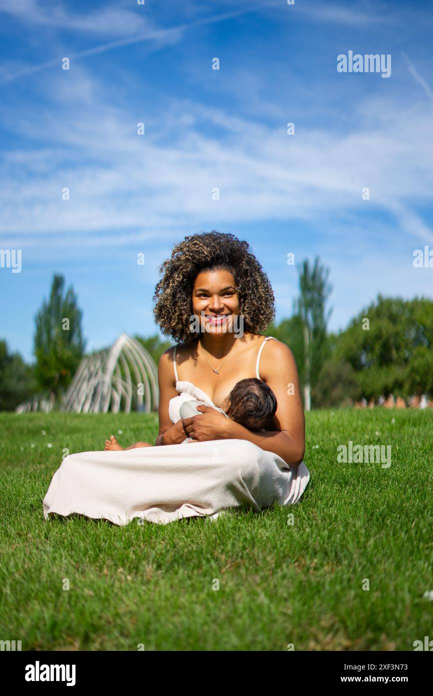 Mère latine souriante allaitant son bébé dans un parc Banque D'Images