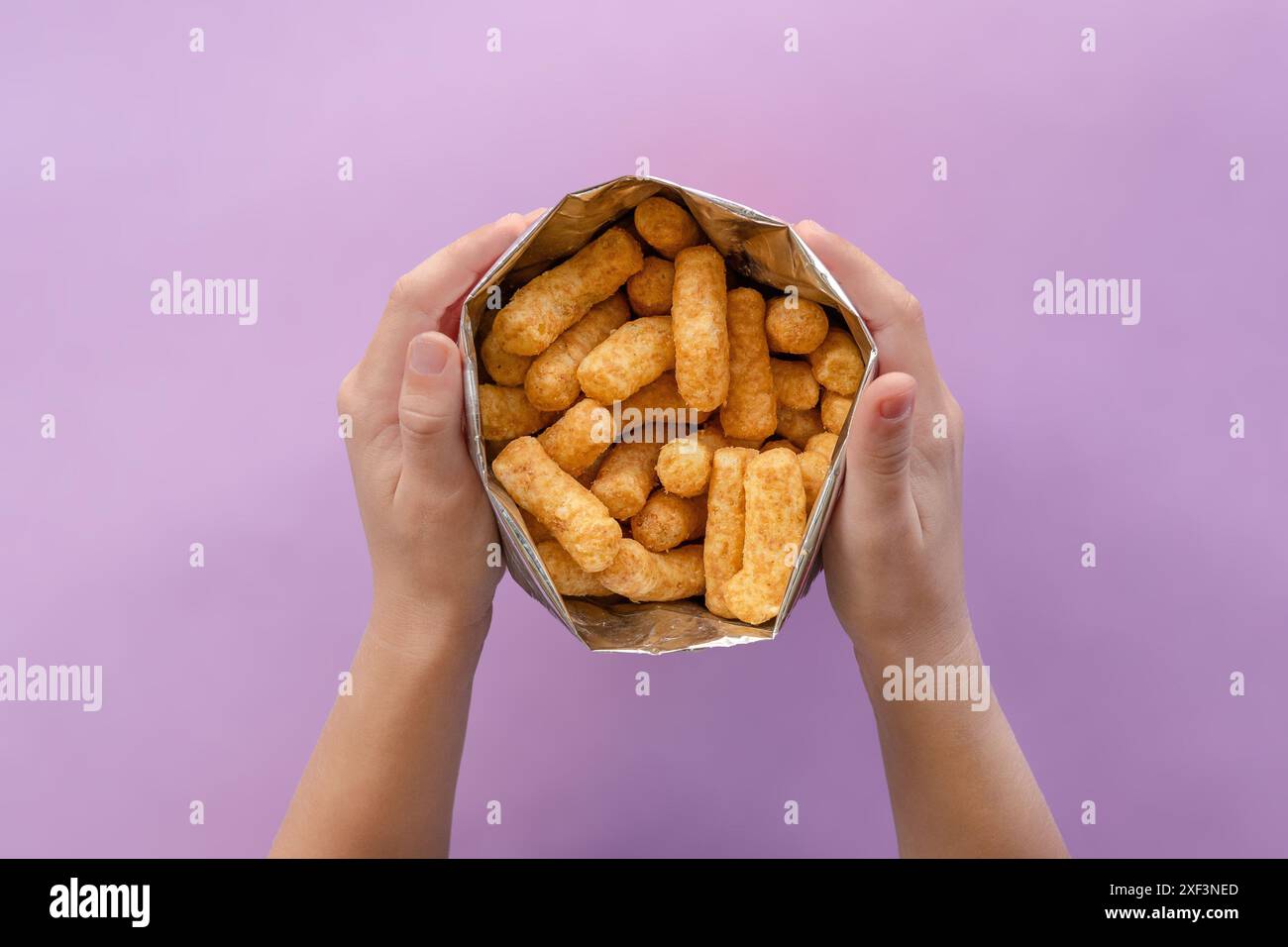 Mains d'enfants tenant le paquet ouvert de Bamba. Bamba est une collation populaire en Israël. Il est fait de puffcorns aromatisés au beurre d'arachide. Gros plan Banque D'Images