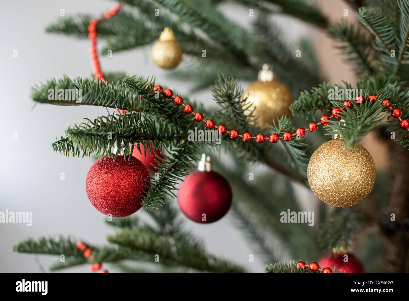 Partie de sapin de Noël décorée de guirlandes, boules rouges et dorées, bokeh Banque D'Images