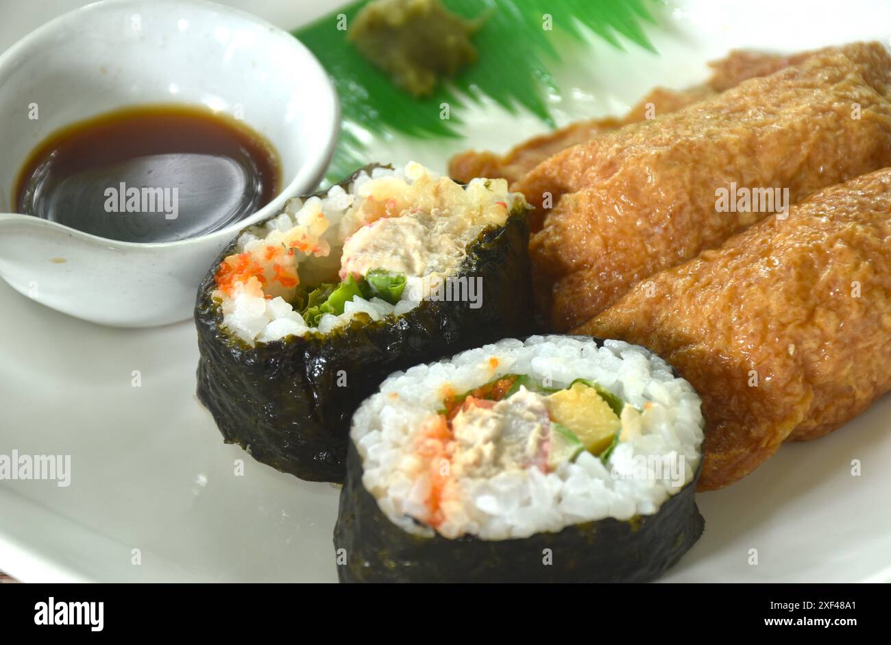 Inari Sushi nourriture japonaise à base de riz enveloppé de tofu frit et de riz maki rouleau d'oeufs sucrés farcis d'algues avec sauce soja wasabi trempant dans l'assiette Banque D'Images