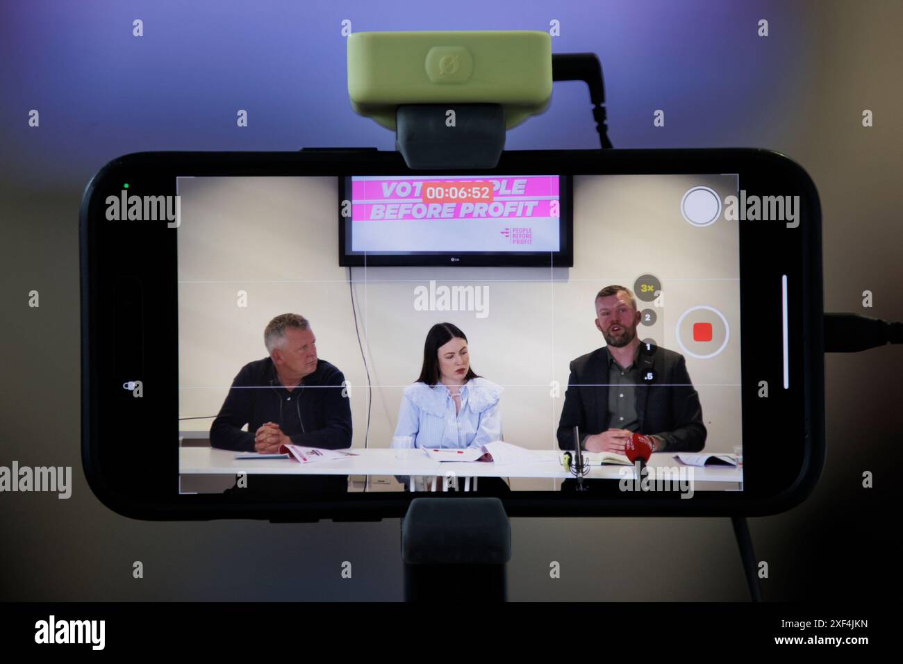 Un iPhone capture une vidéo de personnes devant Richard Boyd Barrett TD de profit (à gauche) avec en partie ses collègues Fiona Ferguson, candidat parlementaire de Westminster pour Belfast North et Gerry Carroll, candidat parlementaire de Westminster pour West Belfast, lors du lancement du manifeste des élections générales pour le parti au Mac Belfast. Date de la photo : lundi 1er juillet 2024. Banque D'Images