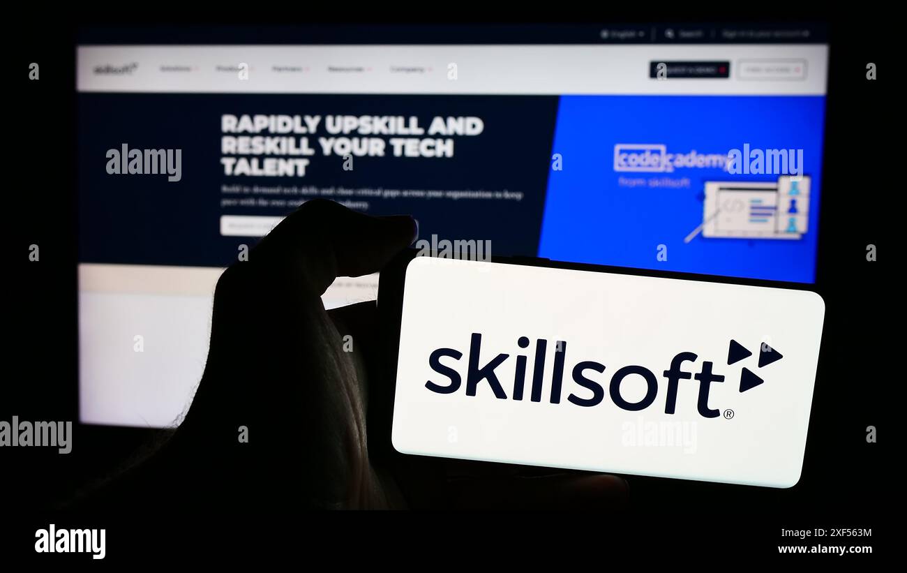 Personne tenant un smartphone avec le logo de la société d'e-learning américaine Skillsoft Corporation en face du site Web. Concentrez-vous sur l'affichage du téléphone. Banque D'Images