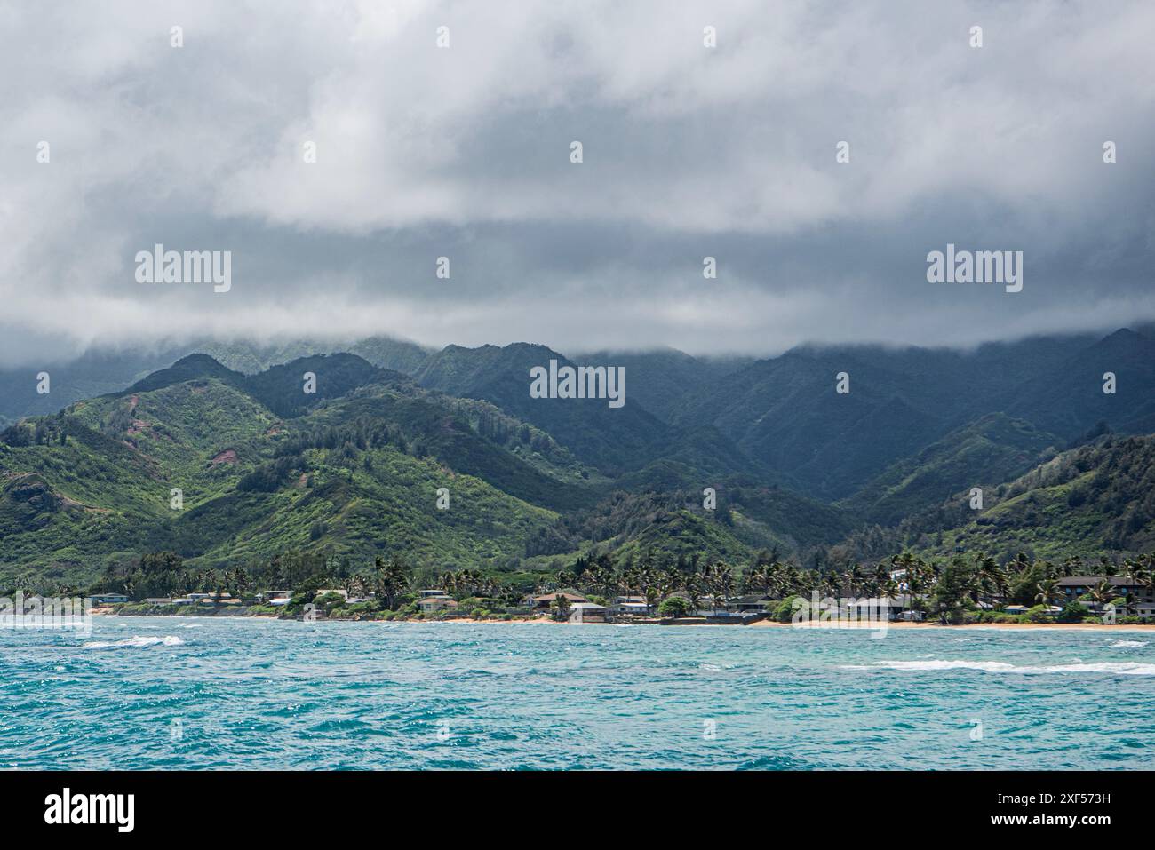 Une vue impressionnante sur le paysage hawaïen avec une mer bleu clair, une plage de sable blanc et d'imposantes montagnes bordées de palmiers. Cette scène encapsulat Banque D'Images