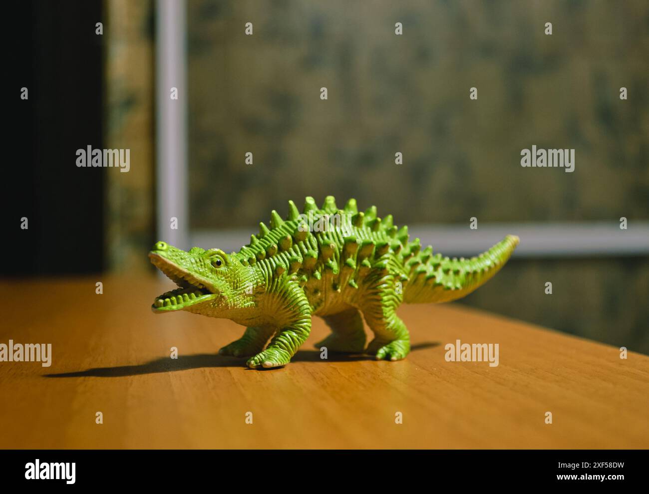 Une figurine d'un dinosaure vert avec des pointes se tient sur une table brune Banque D'Images