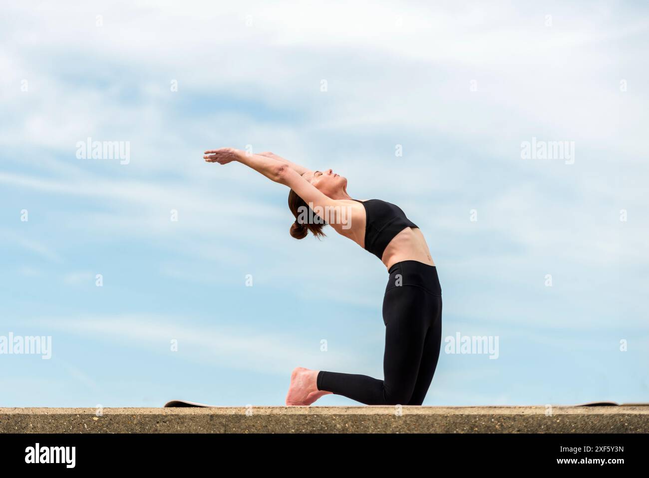 Femme sportive agenouillée faisant un exercice de dos, yoga en plein air Banque D'Images