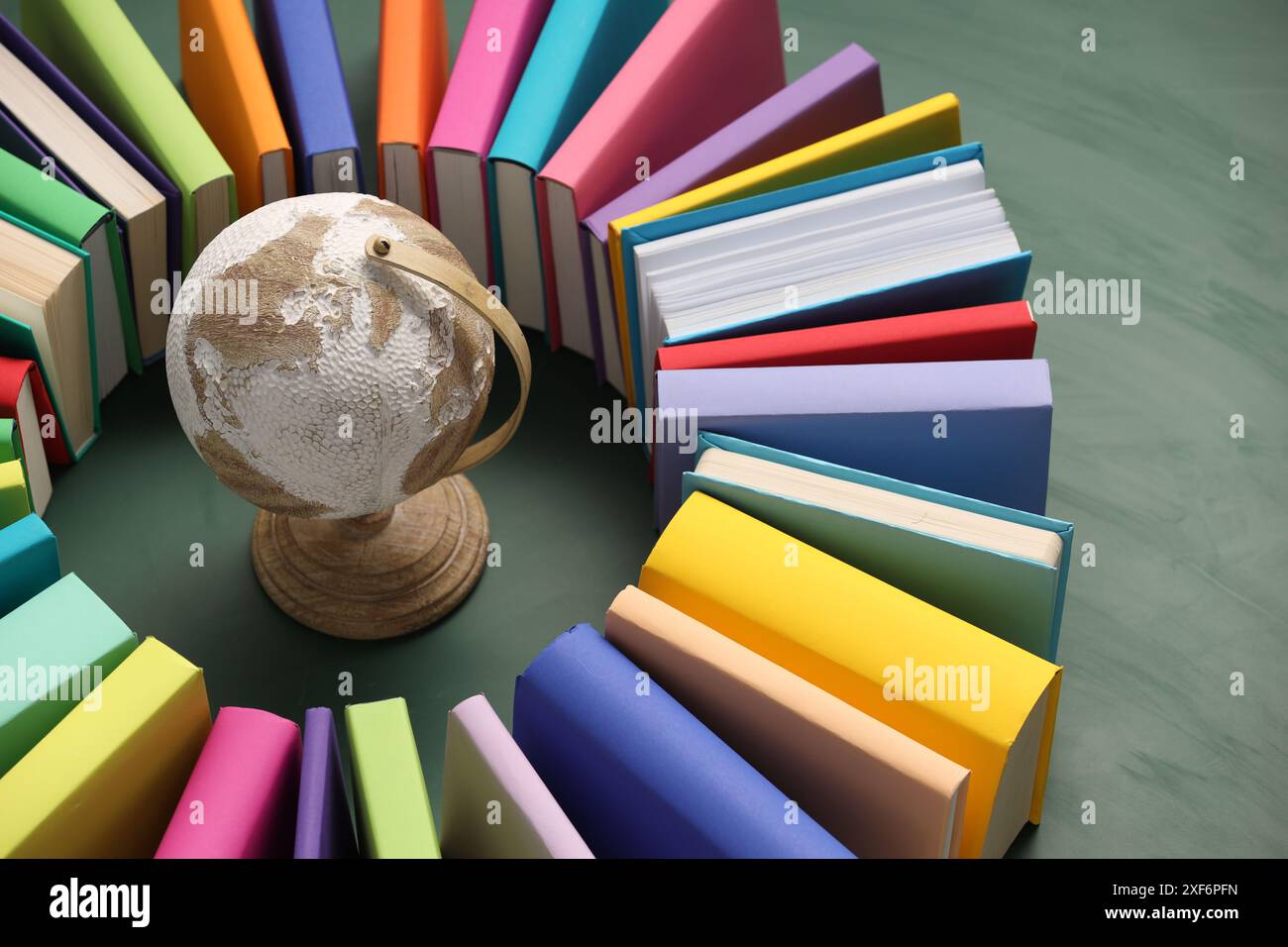 Globe entouré de nombreux livres colorés sur fond vert, gros plan Banque D'Images