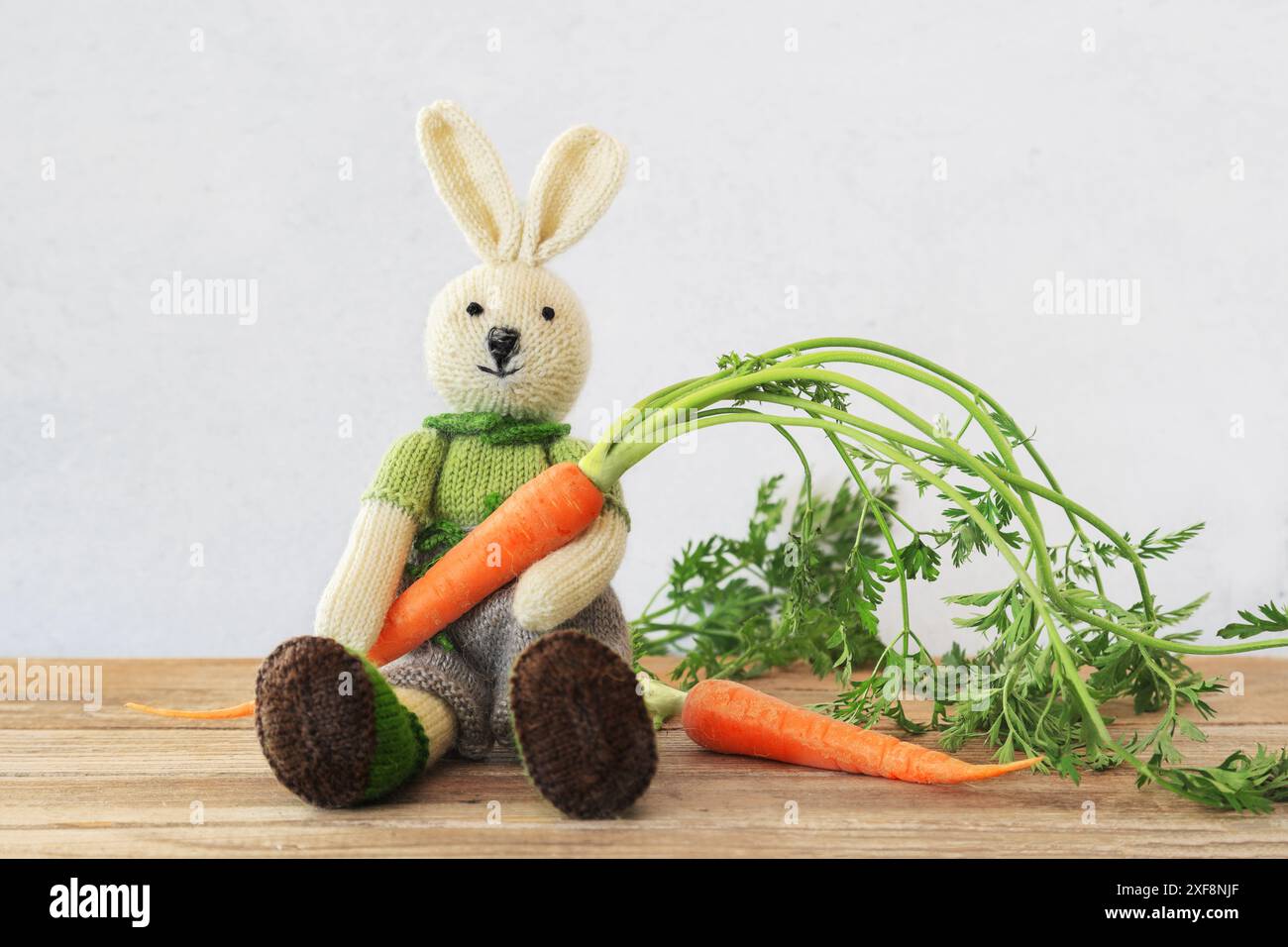 Lapin mignon tricoté assis sur une table en bois tenant une carotte fraîche avec espace de copie Banque D'Images