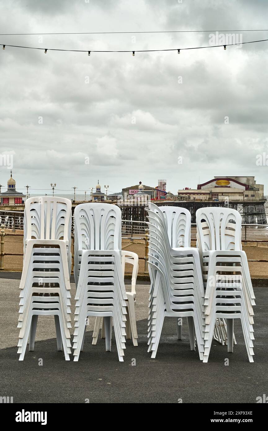 Chaises en plastique blanc empilées sur le front de mer de Blackpool un jour gris froid en été Banque D'Images