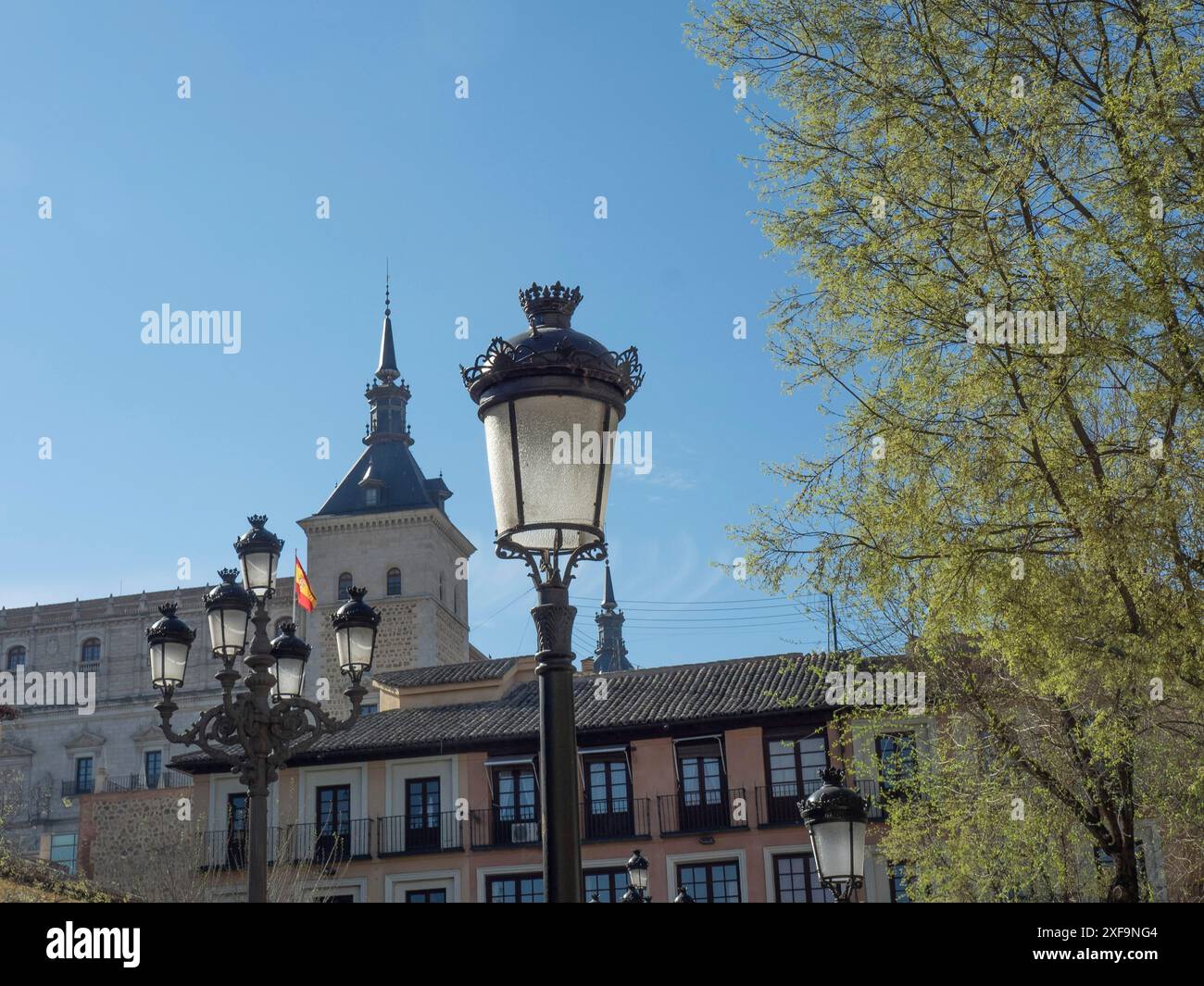 Tour en arrière-plan, façades de maison avec lampadaires au premier plan et un arbre sous un ciel bleu, tolède, espagne Banque D'Images