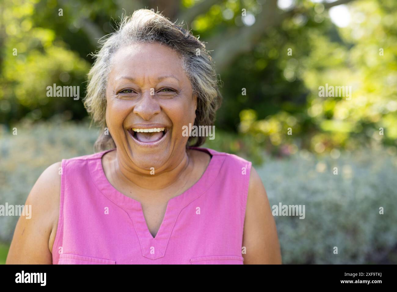 Femme âgée souriante profitant du parc extérieur, portant un haut sans manches rose Banque D'Images