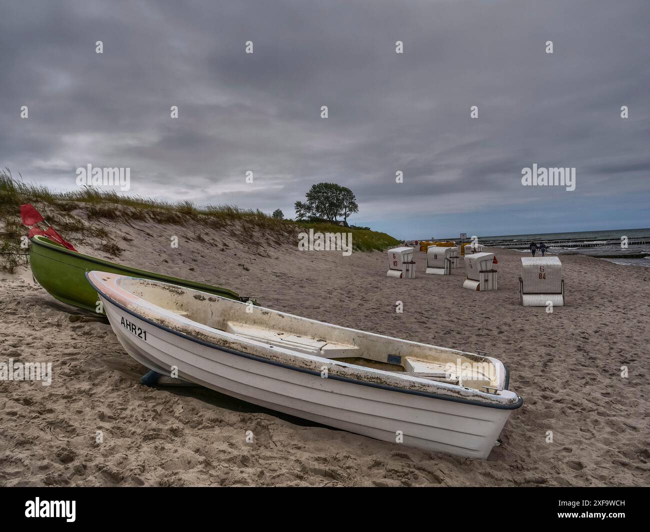 Deux bateaux couchés sur une plage de sable sous un ciel nuageux, avec des chaises de plage vides en arrière-plan, Zingst, mer baltique, allemagne Banque D'Images