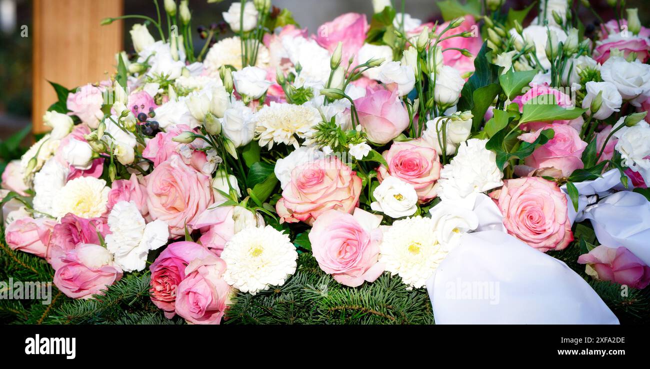 Chrysanthème Rosa fleurs funéraires de roses roses et de chrysanthèmes blancs sur une base de branches de sapin sur une tombe avec une croix en bois en arrière-plan Banque D'Images