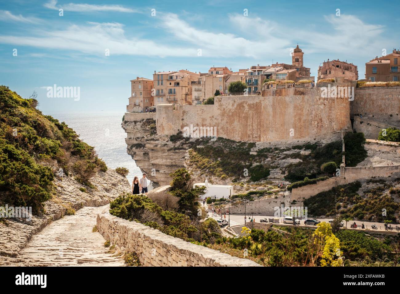 Bonifacio, Corse, France - 28 mai 2024 : un jeune couple monte les marches de pierre devant la citadelle de Bonifacio perchée sur des falaises au-dessus de la Méditerranée Banque D'Images