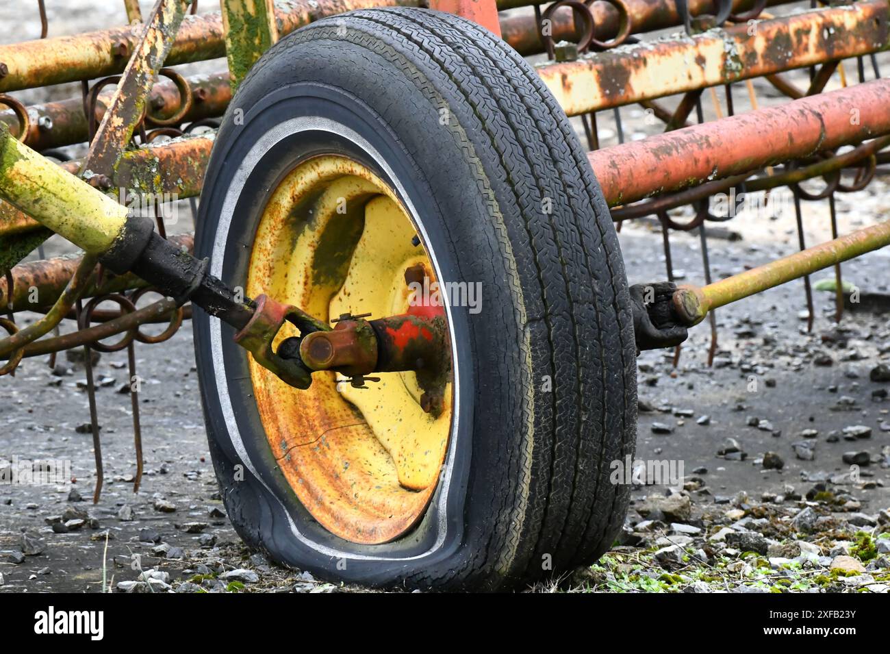L'équipement agricole est à l'arrêt avec un pneu crevé. Le pneu est monté sur une jante jaune qui est rouillée avec l'âge. Banque D'Images