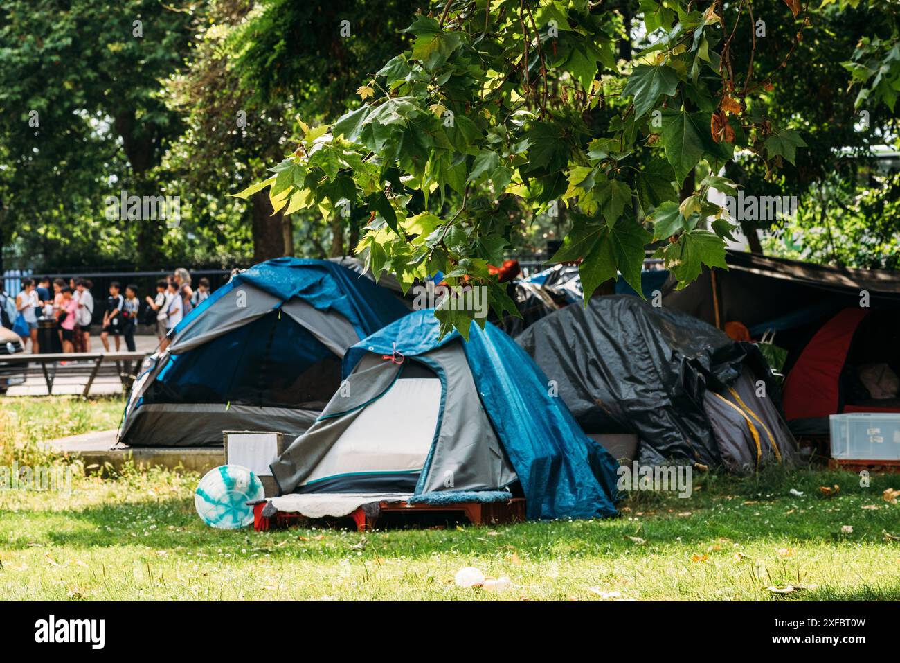 Une collection de tentes et de bâches est installée dans un parc urbain verdoyant. Les tentes sont faites de divers matériaux, y compris la toile bleue, grise et rouge Banque D'Images